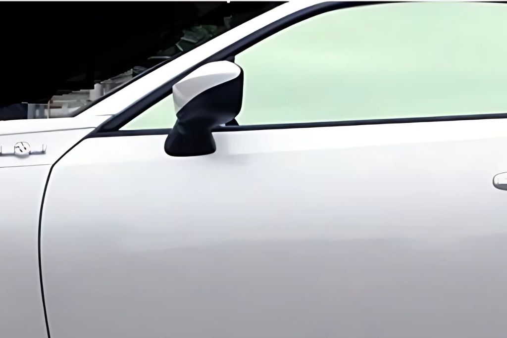 A sleek white car with metalized window tint reflects a subtle metallic sheen. The lightly tinted windows provide strong heat rejection and glare reduction while enhancing the vehicle’s appearance. The side mirror and door handle contrast with the glossy finish of the car's body.