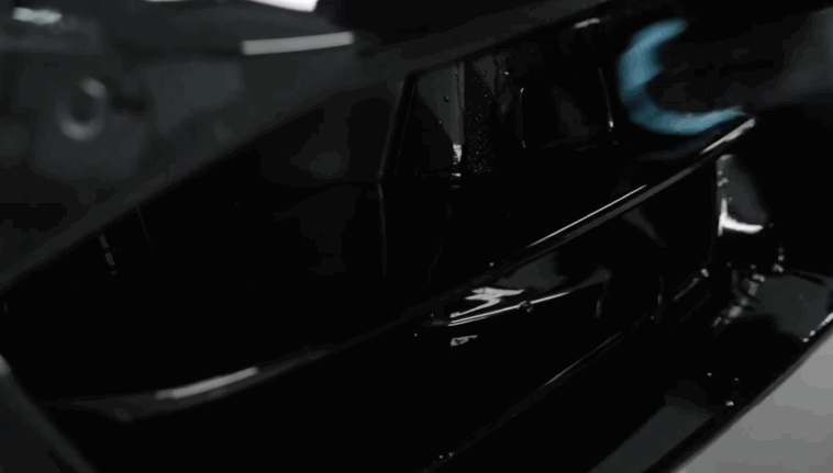 A technician uses a blue detailing cloth to carefully polish the shiny black front grille of a luxury car, emphasizing the vehicle?s high-gloss finish.